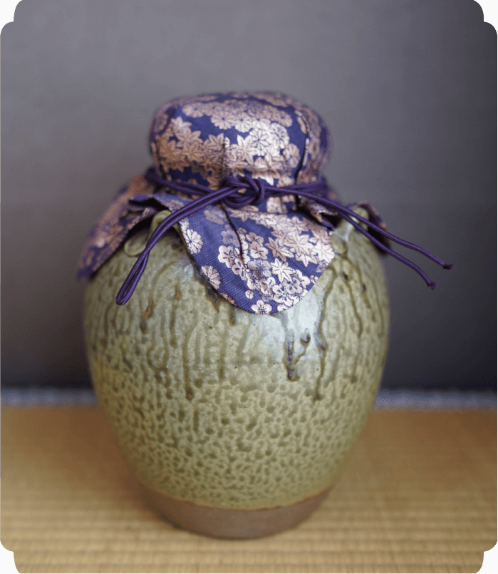 裂地で蓋が包まれた茶入れが畳の上に置かれている